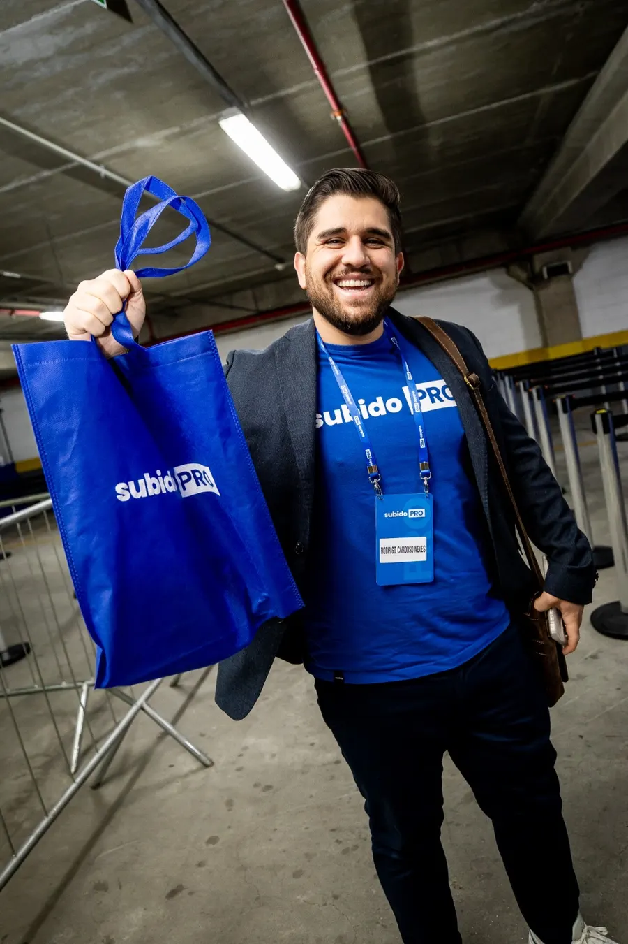 Rodrigo Neves sorrindo em um evento de mentoria, com a sacola do treinamento na mão
